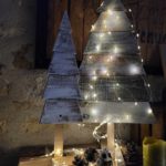 Deux sapins de Noël en bois de réemploi avec une guirlande lumineuse.
