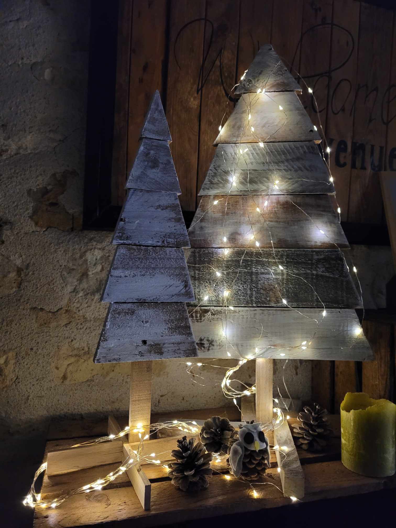 Deux sapins de Noël en bois de réemploi avec une guirlande lumineuse.